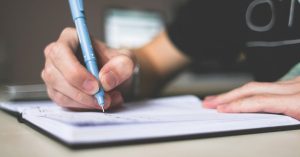 Close-up of hand writing in notebook using a blue pen, focus on creativity.